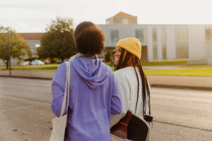 Two teenage black girls chatting and walking down the street together. Black girl with braids holding a skateboard in the city.