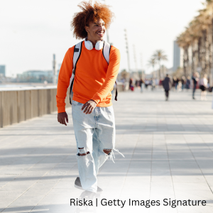 Person with backpack and headphones walking along a waterfront boardwalk on a sunny day.